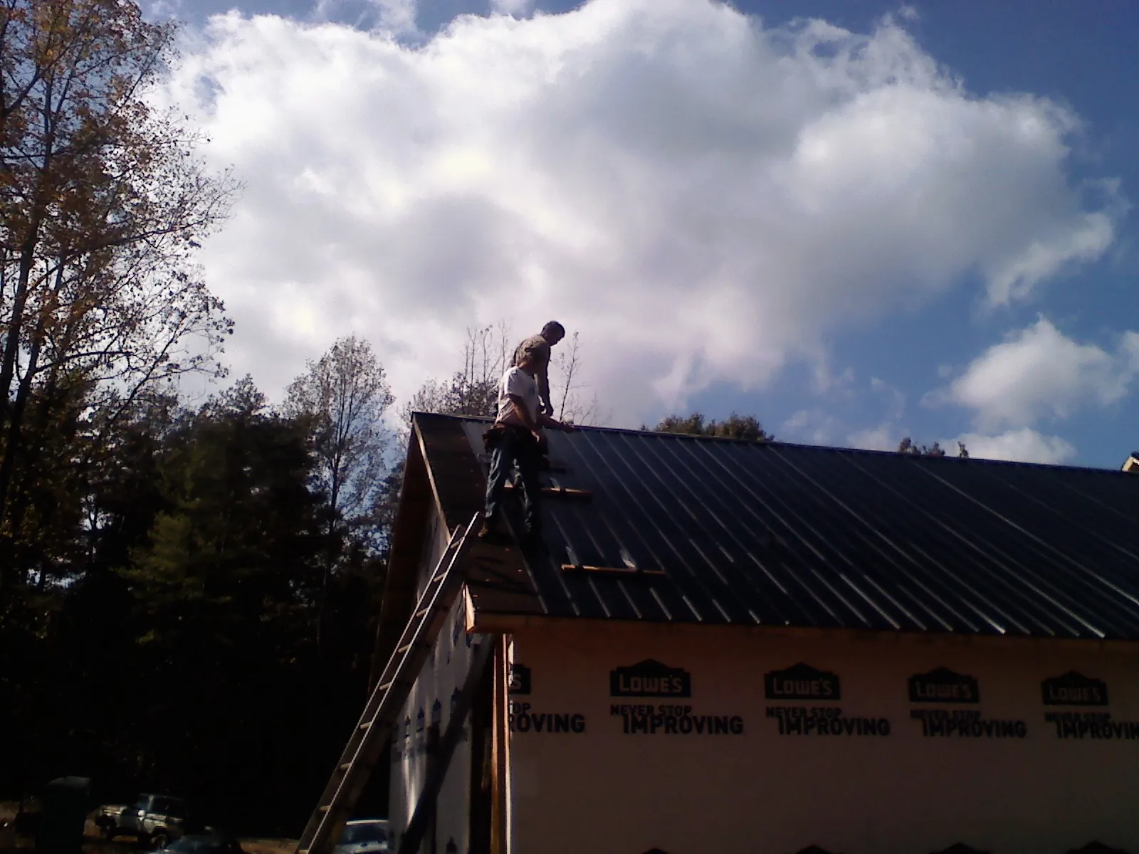 Roofer fastening dark metal panels high against a cloudy sky, from a Roof Inspection job in Worcester