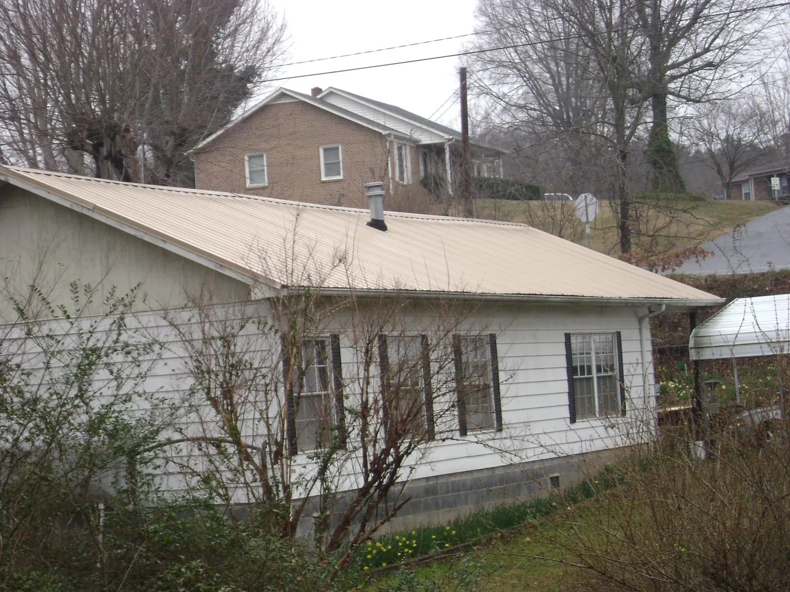 Tan metal roof on a white sided house set into a hillside — Commercial Roofing by Roofing Brothers in Worcester
